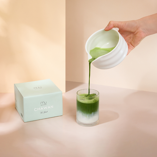 Hand pouring green matcha from the white ceramic Easy Pour Matcha Bowl into a glass of milk, demonstrating its pouring spout.