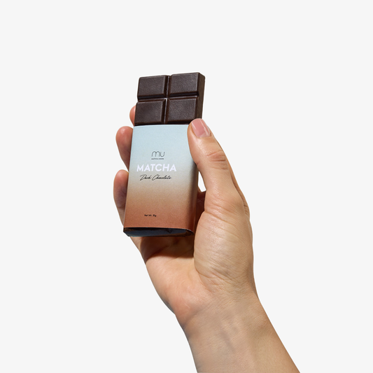 A hand holding a dark chocolate bar wrapped in a silver and peach gradient wrapper against a clean white background.