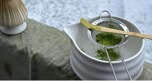 Sifting ceremonial matcha powder into a traditional bowl with bamboo scoop during a calm matcha preparation ritual.