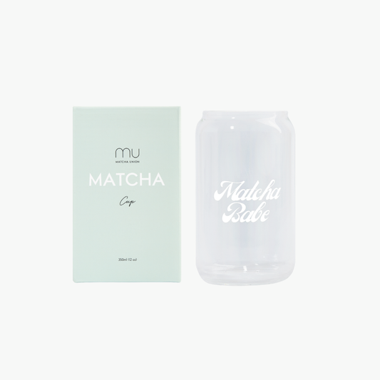 Clear can-shaped Matcha Babe glass with white script lettering beside its mint-green Matcha Union box, designed for iced matcha and cold lattes.