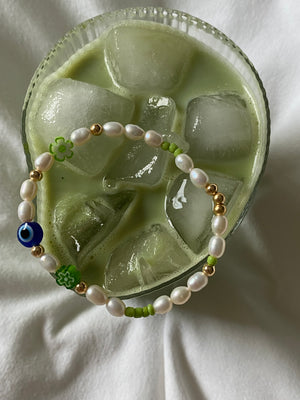 Overhead view of the Matcha Magic bracelet resting across an iced matcha glass, showing its freshwater pearls, gold beads and colourful glass details.