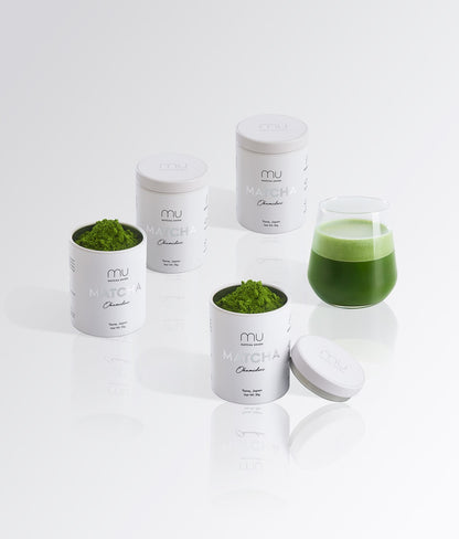 Four Matcha Union Okumidori tins, two open with green matcha powder, beside a glass of prepared matcha.