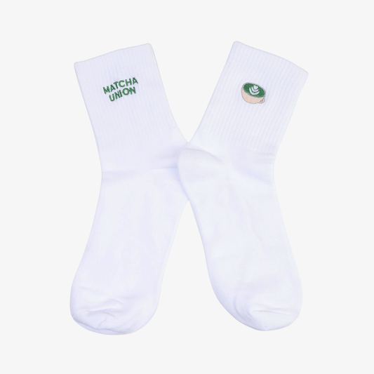Pair of white ribbed Matcha Union socks with green embroidered brand lettering on one sock and a matcha cup design on the other.